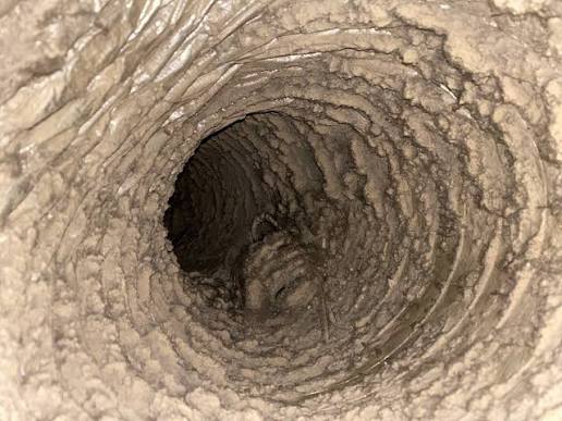 Interior of a round HVAC duct coated with dust and debris in a Raleigh, NC home